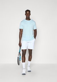 Light blue athletic t-shirt, white shorts, holding a tennis racket, white sports shoes with gray accents, and white crew socks.