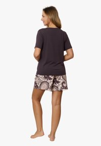 Ciemnoszara koszulka z krótkim rękawem w zestawieniu z beżowymi szortami w wzór paisley. Model stoi boso, widziany od tyłu.