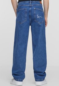 Plati blau lydžiai džinsai, pagaminti iš džinsinio audinio, su klasikinio penkių kišenių dizainu, ryškiomis siūlėmis ir balta siuvinėta logotipu ant galinės kišenės.
