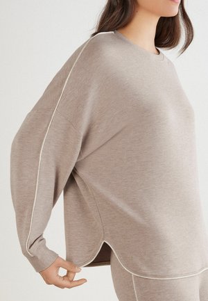 Sweatshirt brun surdimensionné à manches longues, avec un col côtelé et des passepoils blancs contrastants le long des coutures. Détail d'ourlet arrondi.