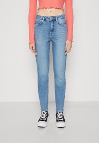 Jeans skinny de color azul claro, hechos de denim, con un diseño de cinco bolsillos y una cintura de altura media, combinados con zapatillas negras y blancas.