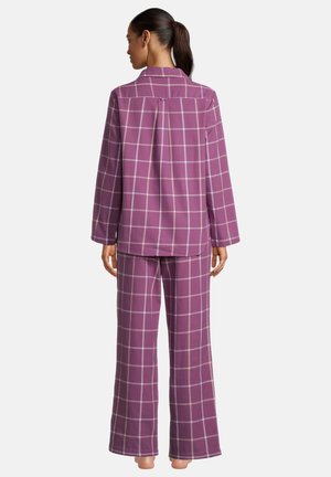 Vrouw staat op blote voeten met de rug naar de kijker, draagt een bijpassend loszittend paarse geruite top met lange mouwen en broek met wijde pijpen.