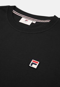 Svart bomullströja med rundad hals, som har en liten broderad FILA-logotyp i röd, vit och blå på vänster bröst.