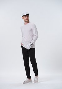 Lyserød langærmet skjorte med struktureret design, sorte bukser, hvid golfhandske og grå sneakers med hvide snørebånd og brune detaljer.