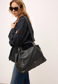 Svart läderhandväska med guldfärgade detaljer, slät textur och en strukturerad form, med avtagbar rem och varumärkeslogotyp.