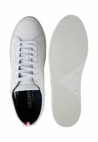 Weiße Leder-Sneaker mit Schnürdesign, strukturiertem Gummisohle und marineblauem Innenfutter. Besitzt dezente Markenlogos und einen gestreiften Akzent an der Ferse.