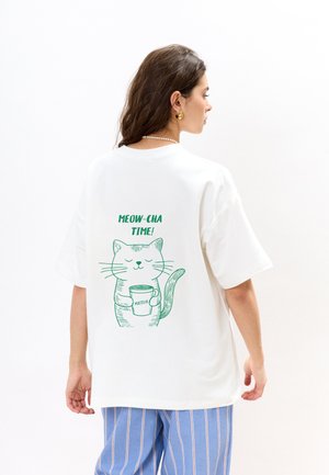 Witte katoenen t-shirt met korte mouwen, voorzien van een groene kat graphic die een beker vasthoudt en de tekst "MEOW-CHA TIME!" op de rug.