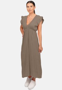 Robe maxi en tissu taupe texturé, avec un décolleté en V profond, des manches volantes et une taille cintrée. Associée à des baskets blanches.