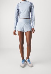 Helles blaues Langarm-Sportoberteil mit strukturierten Seiten, kombiniert mit hellblauen Shorts. Die Schuhe sind hellgrau mit blauen Schnürsenkeln.