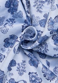 Bloemstof met een blauw en wit kleurenschema, voorzien van gedetailleerde bloemmotieven in verschillende tinten blauw op een lichtblauwe achtergrond.