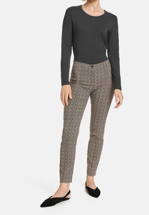 Haut noir à manches longues associé à un pantalon marron ajusté à motif géométrique, ressemblant à du tissu sergé. Porté avec des ballerines noires.