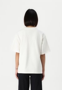 Λευκό βαμβακερό t-shirt με χαλαρή εφαρμογή, κοντά μανίκια και στρογγυλή λαιμόκοψη, εμφανίζεται από τη πίσω πλευρά, με απαλό υφή.