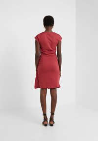 Vestido rojo ajustado con mangas cortas y dobladillo ligeramente asimétrico, hecho de tela suave. Combinado con sandalias negras de tiras.