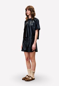 Zwarte top met korte mouwen van namaakleer, gecombineerd met bijpassende korte broek, gedragen met leopardprint ballerina's en crème sokken met strikjes.