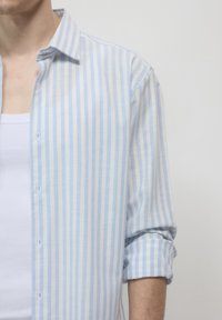 Chemise boutonnée rayée bleu clair et blanche avec une texture de tissu douce et des manches retroussées, présentant un col classique et des boutons à l'avant.