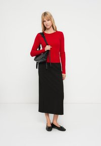 Top rosso a coste a maniche lunghe abbinato a una gonna lunga nera. Borsa a tracolla nera e scarpe basse nere completano il look. Design semplice e lineare.