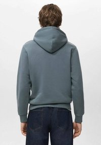 Bluza z kapturem w stonowanym odcieniu zieleni morskiej, charakteryzująca się miękką fakturą, ściągaczami przy mankietach oraz kangurzą kieszenią; zestawiona z ciemnymi jeansami.