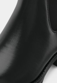 Crna kožna gležnjača s glatkom, sjajnom završnom obradom, sa zaobljenim vrhom i elastičnim bočnim panelima za jednostavno obuvanje. Suptilni detalj šivanja.