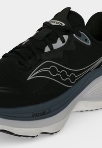 Chaussure de course Saucony noire et grise avec une semelle blanche et un amorti IncrediLUX visible sur le côté.