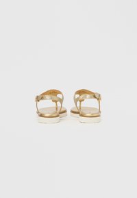 Χρυσά σανδάλια με γκλίτερ, διαθέτουν πίσω λουράκι, επίπεδη σόλα και σταθερή εκρού βάση. Η αγκράφα στο λουράκι προσθέτει μια λειτουργική λεπτομέρεια.