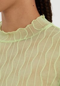 Gjennomsiktig lysegrønn topp med bølgete mønster og scalloped halslinning, med et teksturert stoff som fremhever det intrikate designet.
