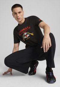Juodas marškinėliai su spalvinga gido lenktyninio automobilio grafika ir užrašu "FORMULA 1 DRIVE TO SURVIVE." Dėvima su juodomis laisvo kirpimo kelnėmis ir sportbačiais.