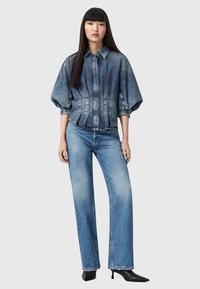 Giacca di jeans con maniche a palloncino, gradiente da blu chiaro a blu scuro, chiusura con bottoni e orlo sfilacciato, abbinata a jeans dritti blu chiaro e tacchi appuntiti.