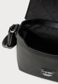 Μαύρη δερμάτινη τσάντα χειρός με υφή στην εξωτερική επιφάνεια, ασημένιο κούμπωμα και λείο εσωτερικό επένδυμα με μοτίβο λογότυπου.