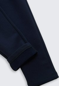 Pantalons en coton bleu marine avec une texture lisse, dotés d'un ourlet replié et de coutures plates, mettant en avant un design simple et fonctionnel.