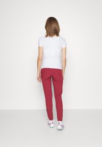 Vit kortärmad topp med scallopade ärmslut, parat med vinröda figurnära byxor. Modellen bär vita sneakers med rosa detaljer.