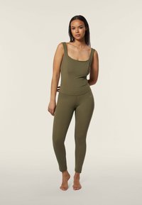 Body verde oliva con scollatura ampia e spalline larghe, abbinato a leggings aderenti coordinati. Materiale liscio e elasticizzato.