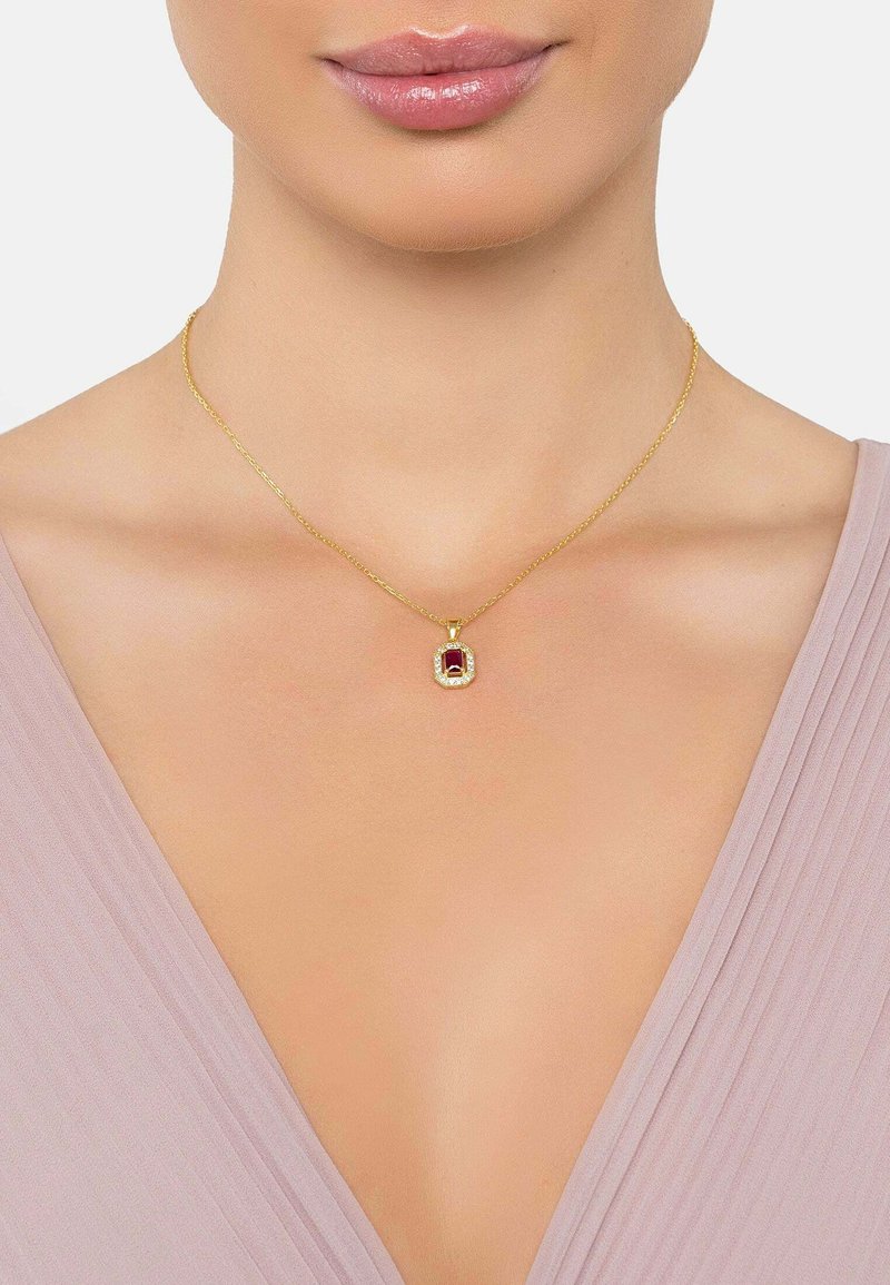 Guldkæde med en rektangulær rød ædelsten vedhæng, omgivet af små klare sten, præsenteret mod en lys baggrund.