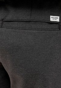 Gros plan d'une poche en tissu noir avec une petite étiquette blanche Jack & Jones cousue au-dessus de l'ouverture de la poche.