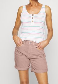 Top de tirantes de canalé a rayas con tres botones, combinado con pantalones cortos de dobladillo enrollado en rosa claro. El top tiene rayas horizontales multicolores.