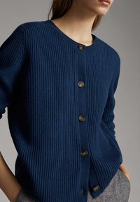 Granatowy kardigan z prążkowanej dzianiny z okrągłym dekoltem, pięcioma brązowymi guzikami oraz luźnym krojem z bocznymi kieszeniami. Miękka tekstura i casualowy design.