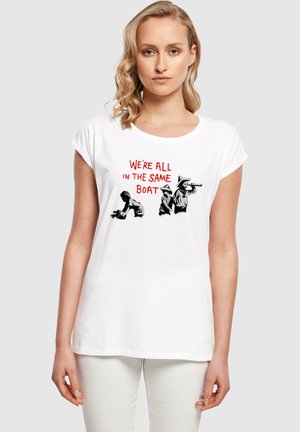 Weißes Baumwoll-T-Shirt mit hochgerollten Ärmeln, versehen mit einer Grafik von drei Figuren und rotem Text, der "WIR SIND ALLE IMSELBEN BOOT" lautet.