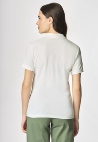 Polo shirt bianco a maniche corte con colletto, tessuto liscio e design aderente, abbinato a pantaloni verde oliva. Aspetto semplice e pulito.
