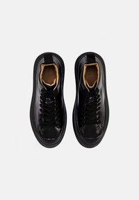 Czarne skórzane sneakersy z teksturowanymi sznurówkami i gładkim wykończeniem. Posiadają okrągły czubek i pętelkę na pięcie, z kontrastowym wnętrzem.