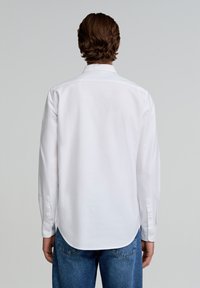 Camisa blanca de manga larga con corte recto, puños abotonados y bajo curvado. Confeccionada en tejido suave, presenta un diseño de cuello clásico.