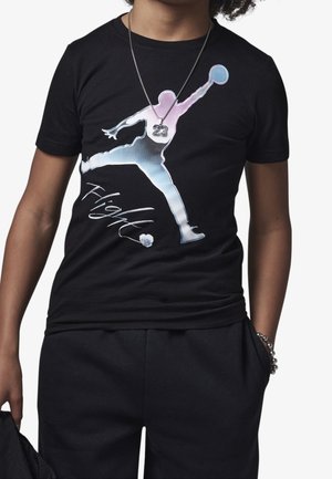 Person iført en sort t-shirt med en stor multicolor silhuet af en basketballspiller og ordet "Flight" foran, bærer også et 23-halskæde.