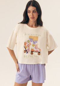 Kremowy krótki t-shirt z grafiką kolorowych wrotków z przodu i fioletowymi szortami; miękki, luźny krój.