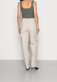 Lichtbeige wijde broek met een elastische tailleband en twee achterzakken. Gecombineerd met een gestructureerde groene gebreide tanktop.