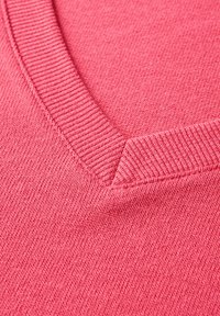 Svetr s výstřihem do V v jasně růžové barvě, který má žebrovaný límec a jemnou pletenou strukturu. Mezi detaily je hladký, rovnoměrný povrch.