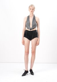 Zwart-wit gestreepte haltertop met een diepe V-halslijn, gecombineerd met hoge zwarte shorts. Model draagt zwarte veterschoenen.