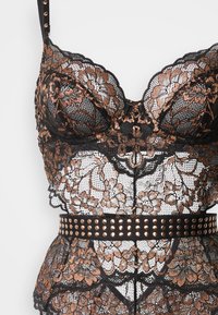 Μαύρο κορσάζ από δαντέλα με χαλκινούς λουλουδένιους σχεδιασμούς· διαθέτει ενισχυμένα φλιτζάνια, ρυθμιζόμενους ιμάντες και μαύρη ζώνη μέσης με καρφιά.