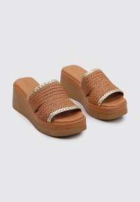 Sandalias de plataforma marrones con parte superior trenzada y acentos dorados. La suela gruesa proporciona altura, mientras que el material texturizado mejora el agarre.