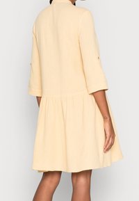 Light yellow dress with a textured fabric, featuring a relaxed fit, three-quarter sleeves, and a flared skirt. Subtle seam details.