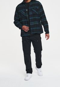 Czarna i niebieska koszula flanelowa w kratę z dwoma kieszeniami na piersi, z przodu na guziki, z długimi rękawami, w połączeniu z czarnymi wąskimi spodniami i białymi tenisówkami.