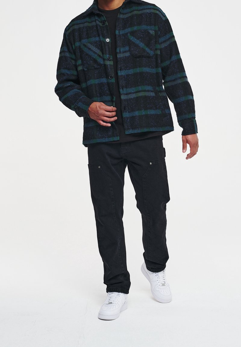 Czarna i niebieska koszula flanelowa w kratę z dwoma kieszeniami na piersi, z przodu na guziki, z długimi rękawami, w połączeniu z czarnymi wąskimi spodniami i białymi tenisówkami.