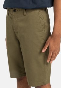 Olivgröna shorts i bomull, med platt framsidan, sidofickor och knäppning med knapp. Slät struktur med rak passform.